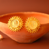 Gold earrings on a terracotta bowl with a warm brown background